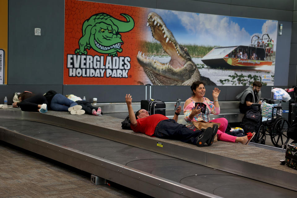 People sitting or lying down at the airport baggage carousel