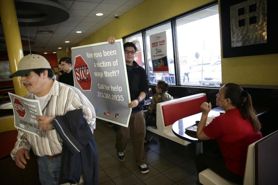 Demonstrators carry banners and signs as they march inside a McDonald's restaurant to protest for higher wages on Tuesday, March 18, 2014, in Huntington Park, Calif. Protesters were set to rally outside McDonald's restaurants in cities including Boston, Chicago and Miami to call attention to the denial of overtime pay and other violations they say deprive workers of the money they're owed. (AP Photo/Jae C. Hong)