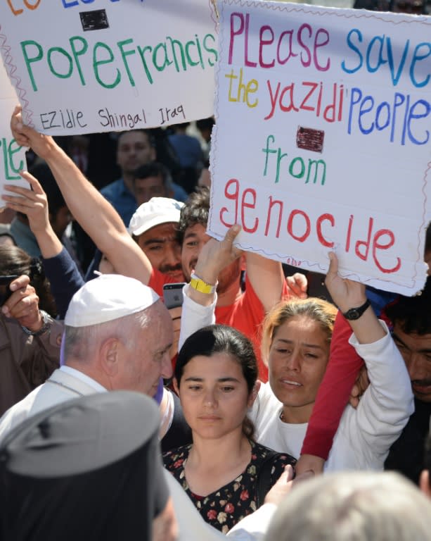 Women hold placards reading "Please save Yazidi people from genocide" as Pope Francis greets migrants at the Moria refugee camp on April 16, 2016