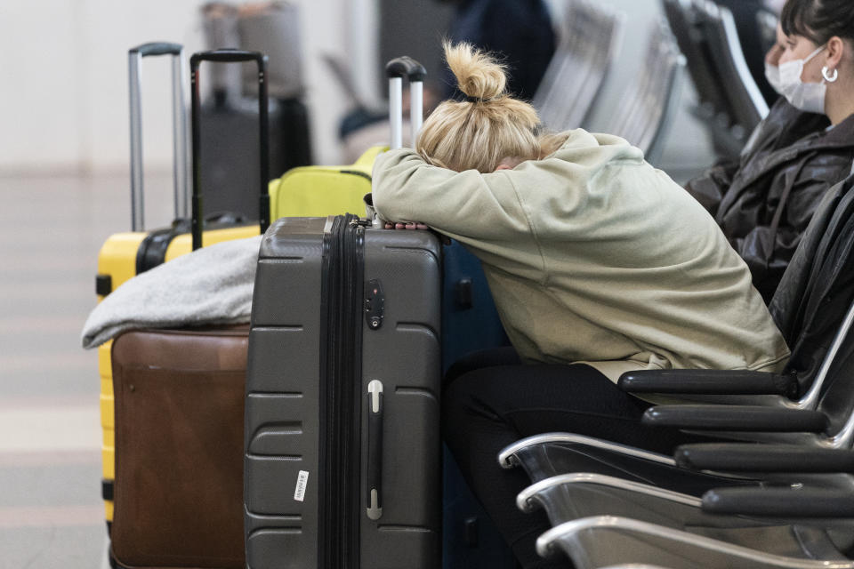 Jessica Andrijauskas, from Buenos Aires, rests her head on her luggage as she awaits the results of her COVID-19 test, at Ronald Reagan Washington National Airport, Wednesday, Dec. 29, 2021, in Arlington, Va. Winter weather and crew members infected with COVID-19 have forced airlines to spike thousands of U.S. flights over the past week, complicating travel plans for many people during the busy holiday season. It’s not clear when travel will return to normal, but airlines say a recent move by U.S. public health officials should help get workers back sooner. (AP Photo/Alex Brandon)