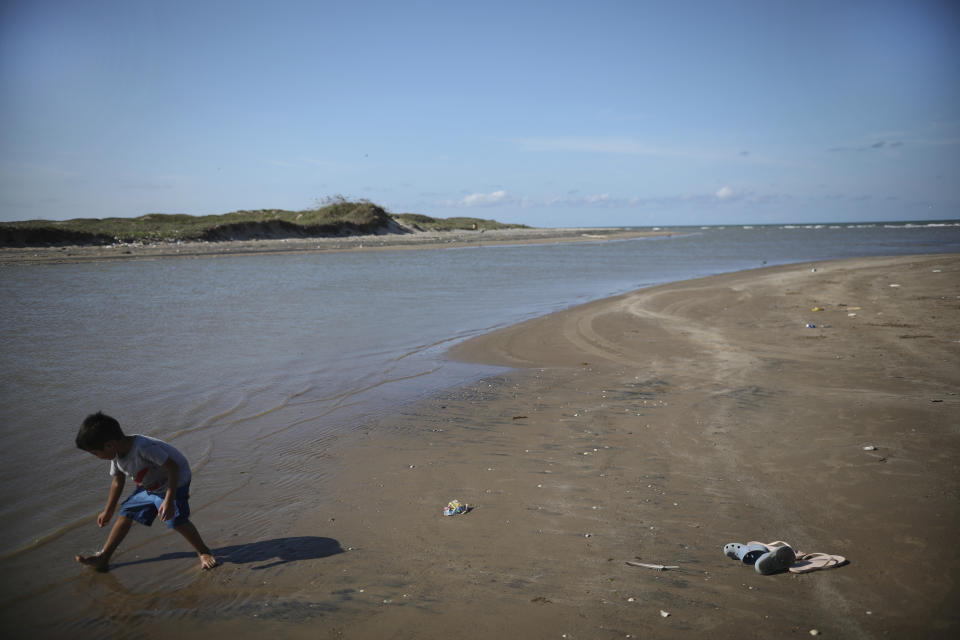 In this Aug. 2, 2019 photo, a child collects seashells as he walks along the shoreline in Playa Bagdad close to the mouth of the Rio Grande where between the U.S. and Mexico lies an expanse of water, perhaps 25 yards (meters) wide, so shallow that you can walk across at low tide, but few people do. (AP Photo/Emilio Espejel)