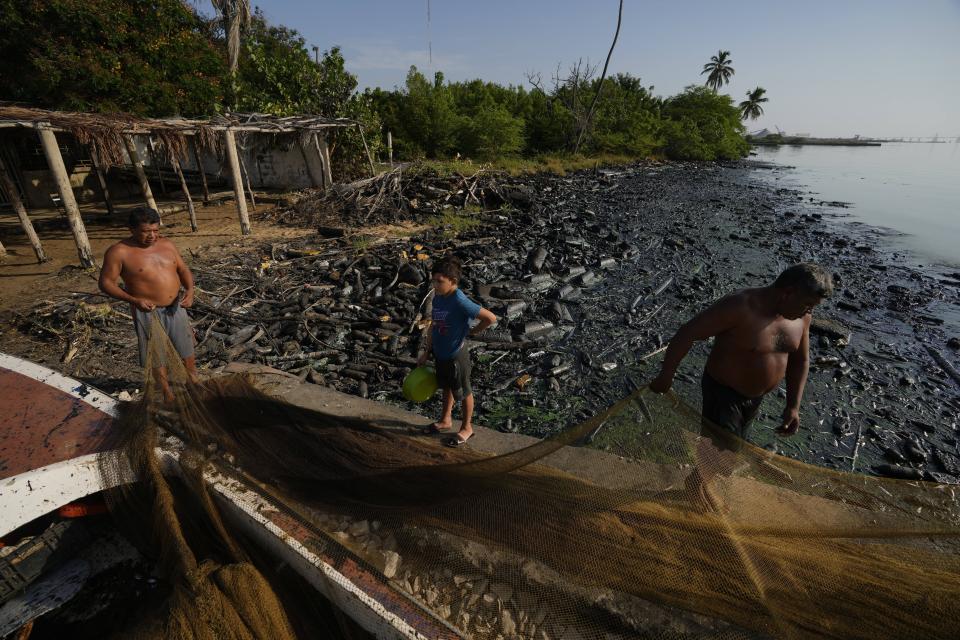 Fishermen spread out their net on the banks of Lake Maracaibo contaminated with oil and trash, in San Francisco, Venezuela, Wednesday, Aug. 9, 2023. The pollution around the lake, one of Latin America's largest, is the result of decades of excessive oil exploitation on its bed, inadequate maintenance, and a lack of investment to improve an already obsolete infrastructure, according to environmentalists. (AP Photo/Ariana Cubillos)