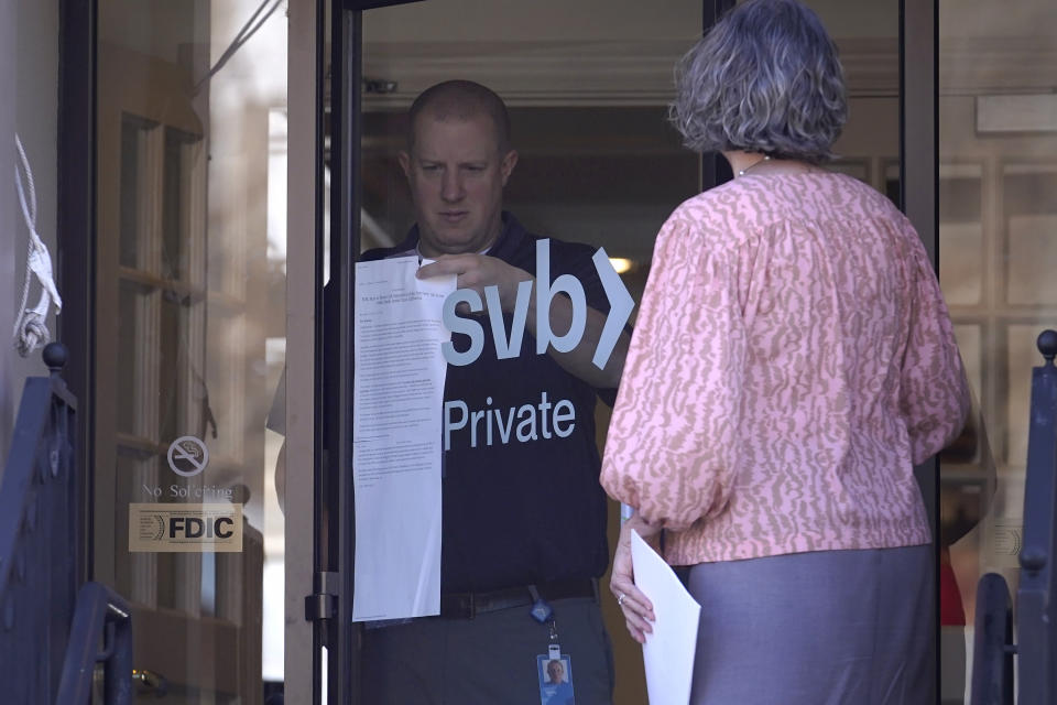 A person removes a paper notice from a glass door at the Silicon Valley Bank branch location, in Wellesley, Mass., Monday, March 27, 2023. North Carolina-based First Citizens will buy Silicon Valley Bank, the tech industry-focused financial institution that collapsed earlier this month. (AP Photo/Steven Senne)