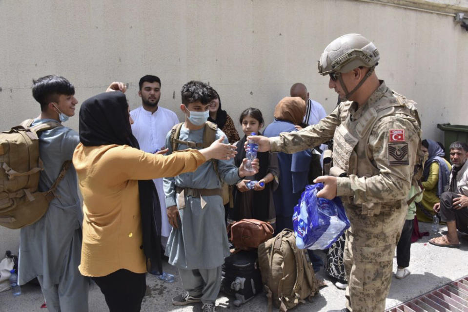 A Turkish soldier offers water to Turkish nationals waiting to board a Turkish Air Force plane at Kabul airport, Afghanistan, Wednesday, Aug. 18, 2021. Turkey's defense ministry says a Turkish Air Force plane has ferried some 200 Turkish citizens from Kabul to Pakistan as nations continue to evacuate their citizens after the Taliban took control of Afghanistan.(Turkish Defense Ministry via AP)