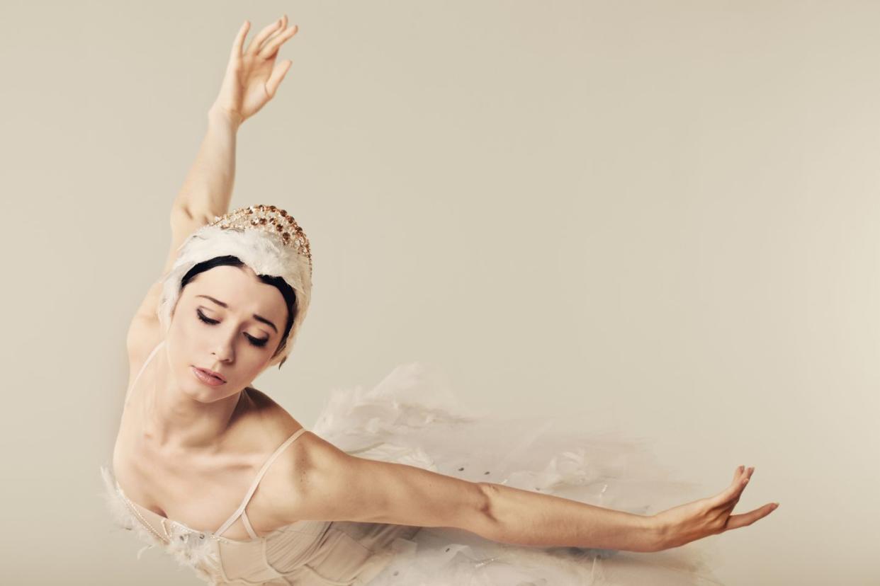 classical ballerina in white tutu and headdress in a graceful position with arms back and one upward and head pointed down