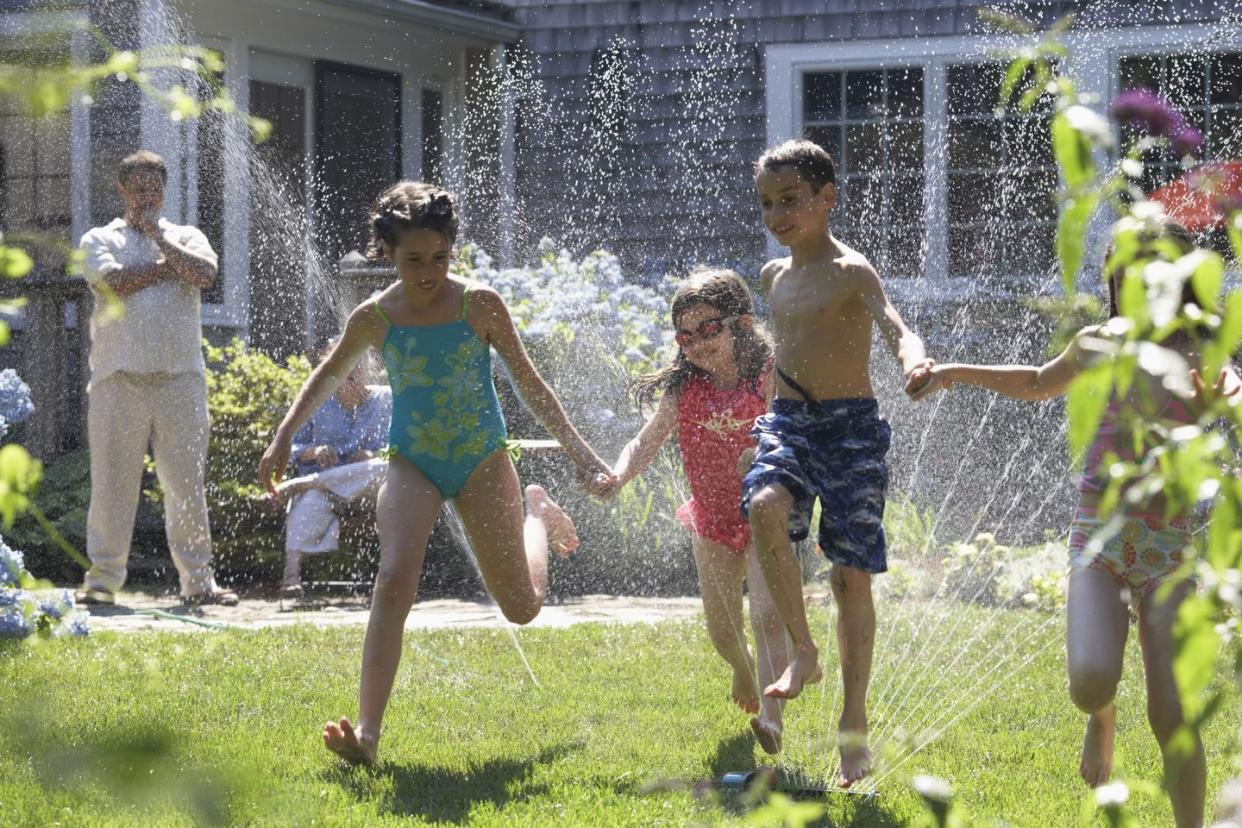 group of four children playing around a sprinkler in a garden on 4th of july