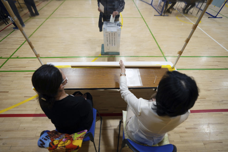 Representatives of a local election administration commission watch voters casting their ballots as they cast their votes for the lower house elections at a polling station Sunday, Oct. 31, 2021, in Tokyo. (AP Photo/Eugene Hoshiko)