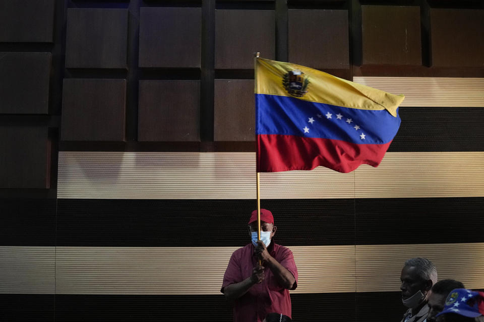 A supporter of the ruling socialist party waves a Venezuelan flag on the sidelines of a press conference by former Foreign Minister Jorge Arreaza who conceded the previous day's gubernatorial re-run election to opposition candidate Sergio Garrido in Barinas, Venezuela, Monday Jan. 10, 2022. (AP Photo/Matias Delacroix)