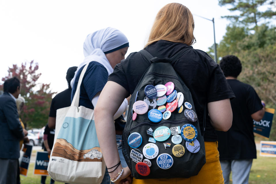 Two women, one in a head covering, the other with a backpack covered in metal political buttons, stand in line. (Megan Varner/Getty Images)