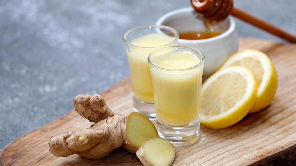 Clear glasses of ginger shots next to ginger, lemon and honey