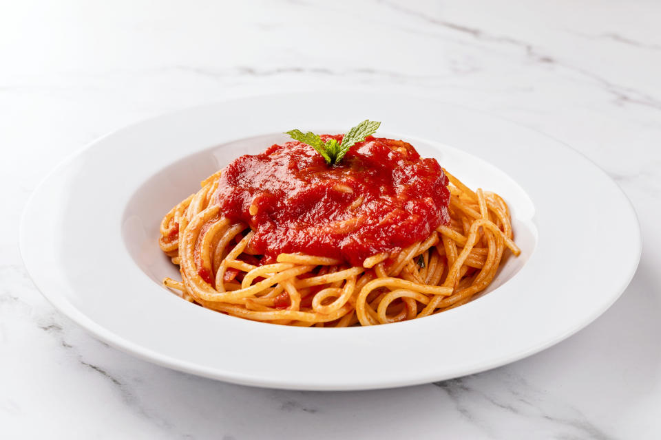 A plate of spaghetti topped with tomato sauce and garnished with a sprig of mint on a marble surface