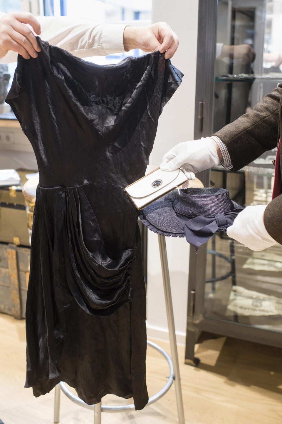 In this Wednesday, Nov. 20, 2019 file photo an employee hold a cocktail dress, a wallet and a straw-hat that belonged to Eva Braun the wife of Adolf Hitler prior to an auction in Grasbrunn near Munich, Germany. A Geneva businessman says he has purchased Adolf Hitler's top hat and other Nazi memorabilia to keep them out of the hands of neo-Nazis and will donate them to a Jewish group. (Matthias Balk/dpa via AP)