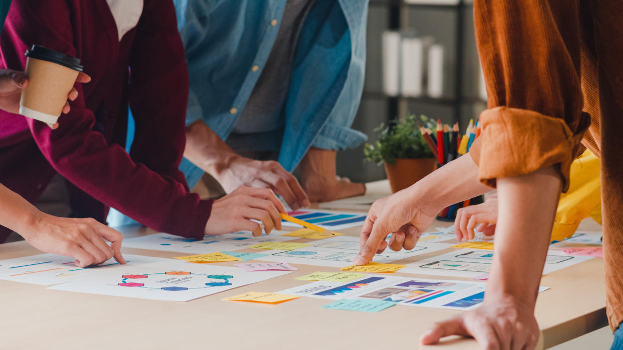 Asian entrepreneurs and businesswomen meet, exchange ideas on creative web design application and develop template layout for mobile phone design while working together in small office.