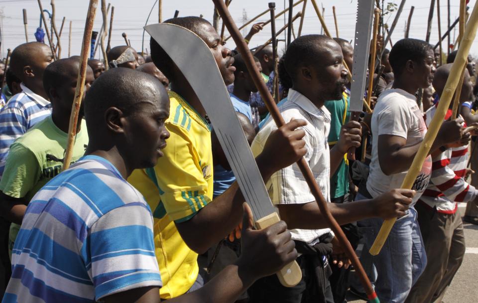 Striking mine workers armed with machetes, sticks, and spears march to a smelter plant at the Lonmin Platinum Mine near Rustenburg, Wednesday, Sept, 12, 2012 to hand over a memorandum to mine management and to ensure that workers had not reported for duty. Miners are refusing to return to work until their demands over low pay and working conditions are met. Strikes are spreading to nearby gold mines. (AP Photo/Denis Farrell)