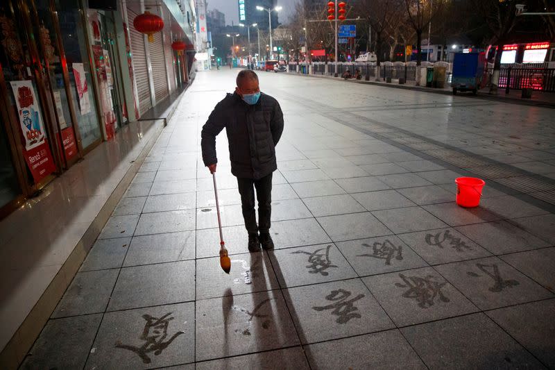 A man wears a face mask as he practices calligraphy of Chinese characters on a pavement in Jiujiang