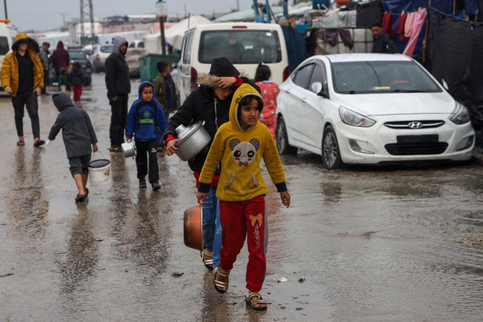 Displaced Palestinians walk through the rain to get food rations at a makeshift tent camp in Rafah (AFP via Getty Images)