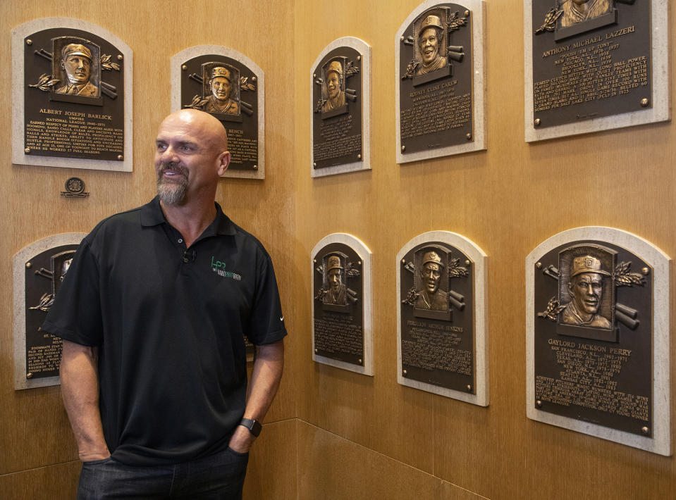 In this photo provided by the National Baseball Hall of Fame and Museum, Larry Walker poses near the wall of plaques, Tuesday, Feb. 25, 2020 at the National Baseball Hall of Fame in Cooperstown, N.Y. Walker said on Tuesday that his Hall of Fame plaque will show him in Colorado Rockies cap, not a Montreal Expos hat. He added the key to picking the Rockies is that Colorado was "where the majority of my damage was done." (Milo Stewart, Jr./National Baseball Hall of Fame and Museum via AP)