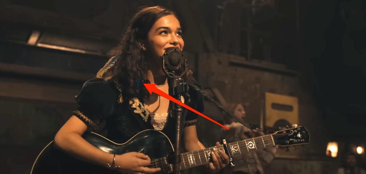 Lucy Gray holds a guitar and sings with a feather in her hair in "The Hunger Games" prequel movie.