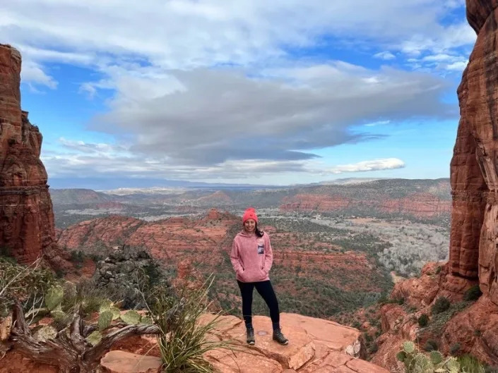 A woman standing at a scenic viewpoint over red rock formations.