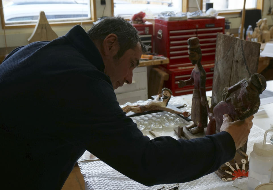 Victor Goler adjusts a holy family sculpture group in his studio outside Taos, New Mexico, Friday, April 14, 2023. As a conservator and master santero – an artist trained in New Mexico's centuries-old tradition of religious sculpture and painting – Goler has worked on many historic and imperiled churches, helping to conserve their distinctive artistic patrimony. (AP Photo/Giovanna Dell'Orto)