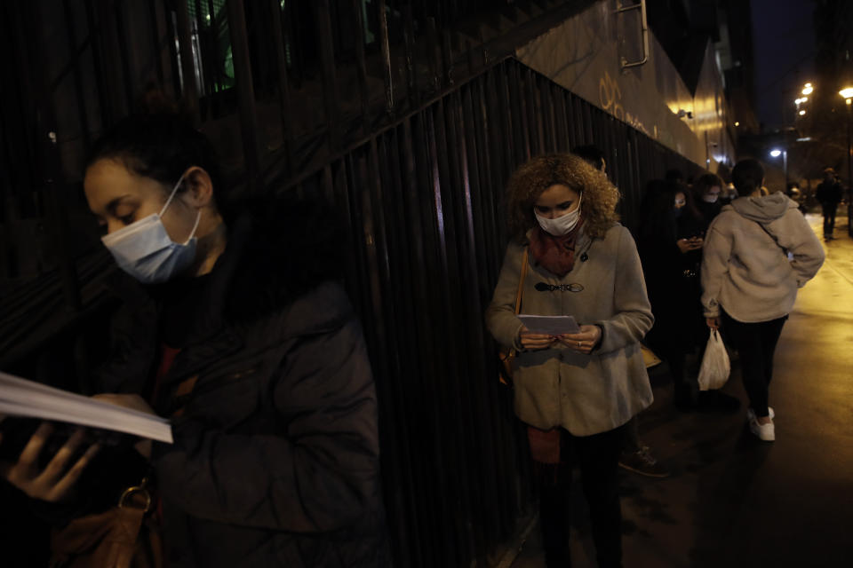 Leila Ideddaim, a student in hotel and restaurant management, center, reads as she lines up for free food aid organized by Linkee, a Paris-based company collecting food waste in Paris, Thursday, Feb. 4, 2021. The 21-year-old student in hotel and restaurant management has seen her plans turned upside down by the virus crisis: With restaurants and tourist sites shuttered and France under a 6 p.m. curfew, her career prospects are uncertain and odd jobs that were supposed to keep her going during her studies hard to come by. (AP Photo/Christophe Ena)