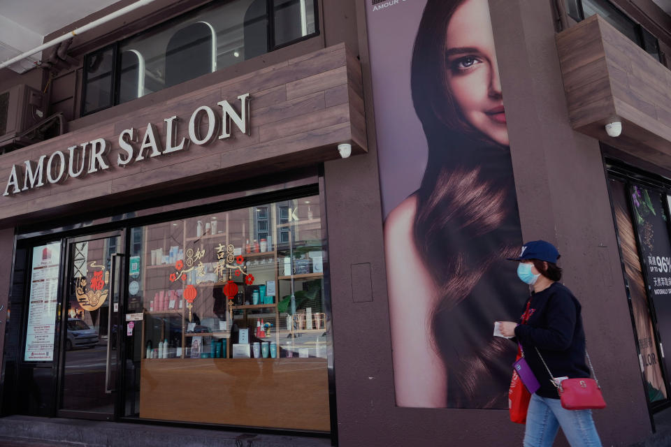 A woman wearing a face mask walks past a temporarily closed hair salon in Hong Kong, Thursday, March 10, 2022. (AP Photo/Vincent Yu)