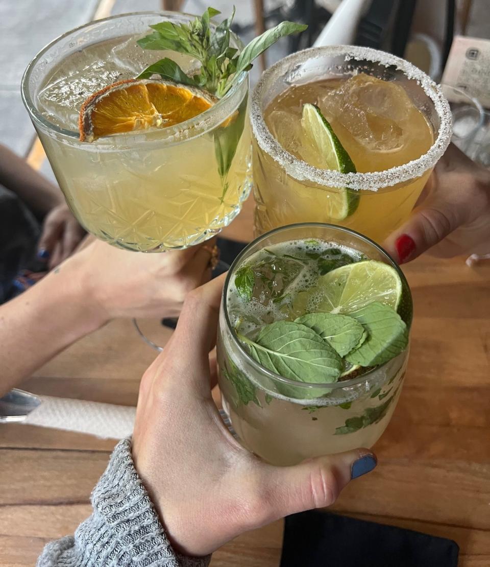 Hands holding three cocktails.