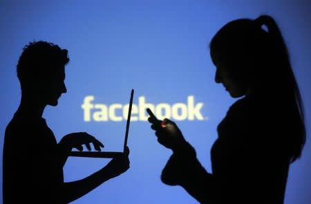 People are silhouetted as they pose with laptops in front of a screen projected with a Facebook logo, in this picture illustration taken in Zenica October 29, 2014. REUTERS/Dado Ruvic