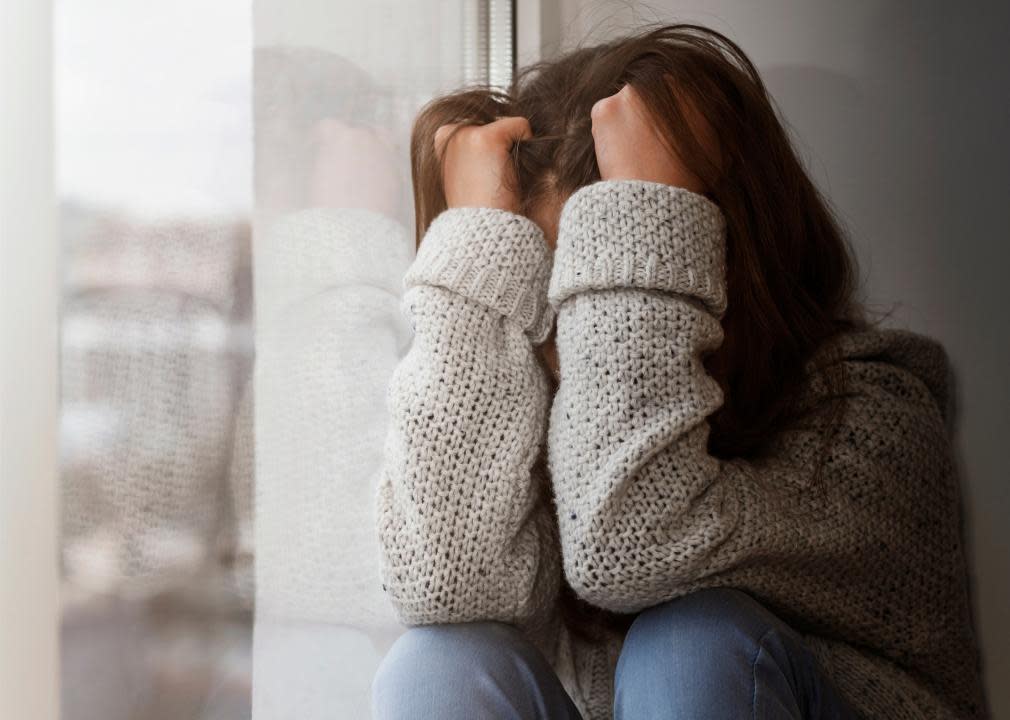 Teen sitting against a wall with her arms covering her face.