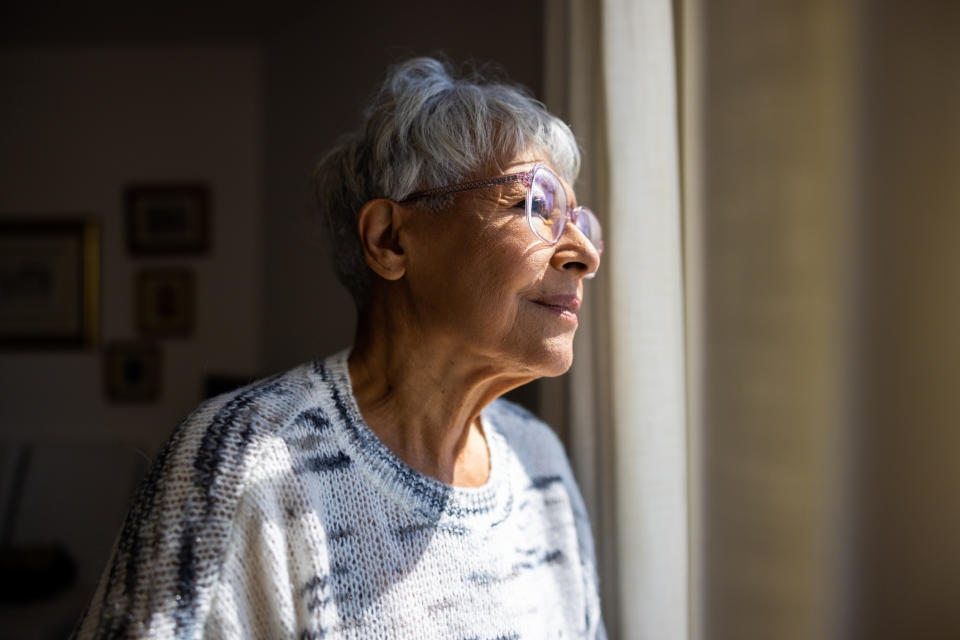 O persoană în vârstă care poartă o jachetă se uită pe fereastră cu o expresie reflectorizată