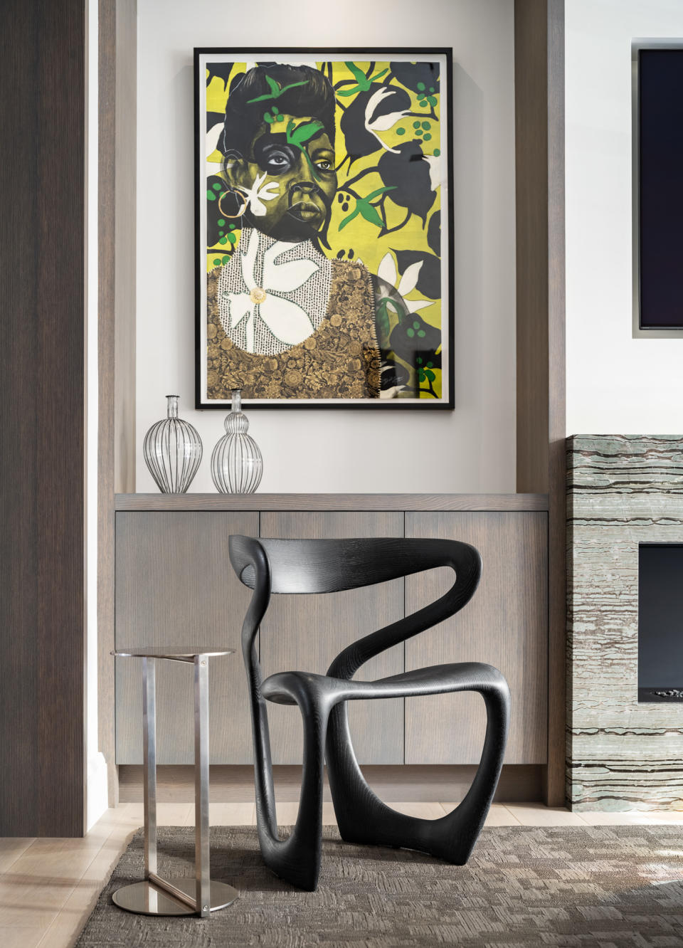 A grey living room with yellow, green and black artwork and a single black wood armchair