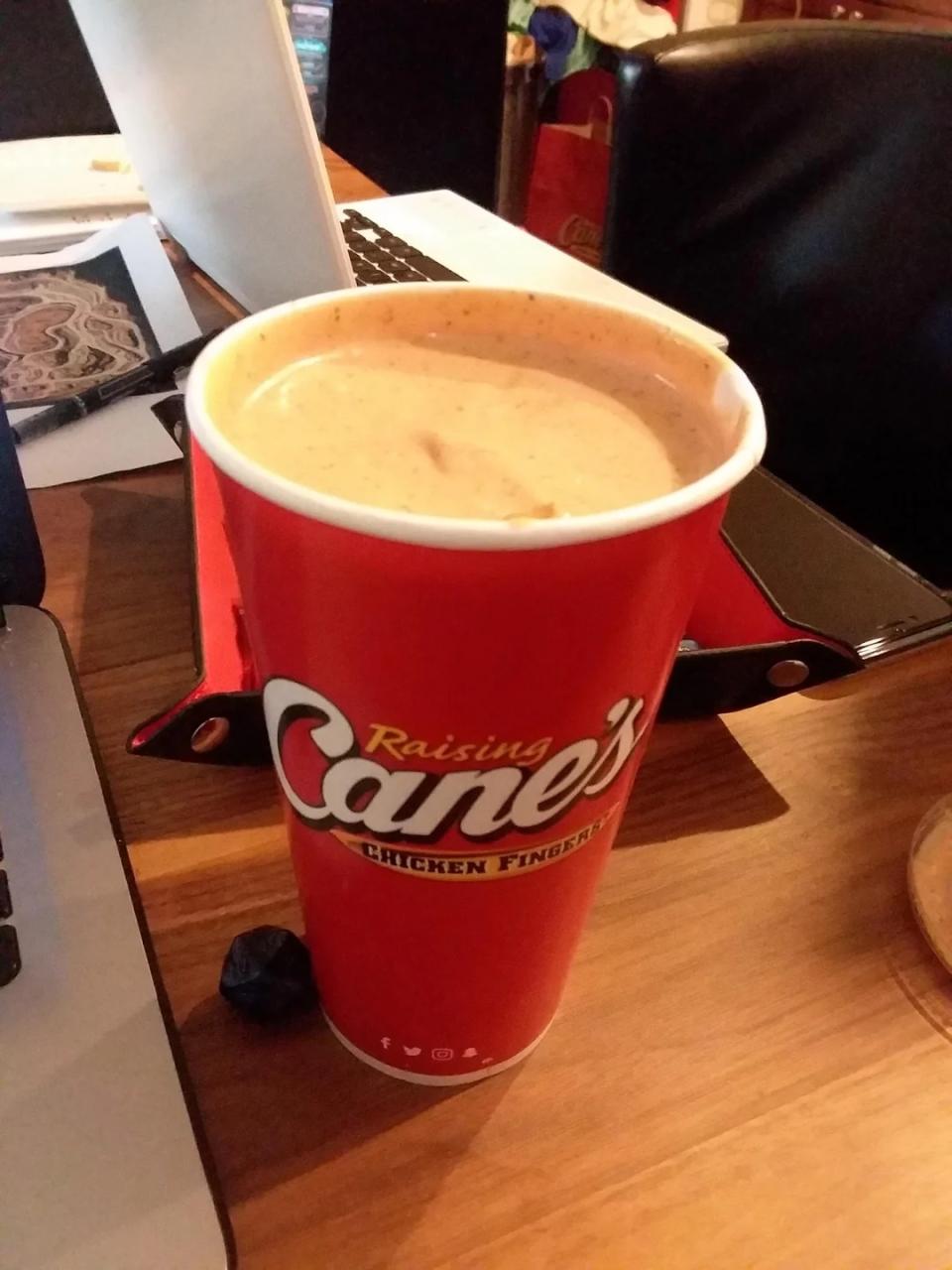He places Cane's sauce-filled cup on a desk, with a laptop in the background