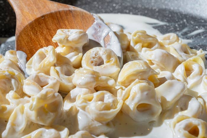 A plate of cooked tortellini pasta with a wooden spoon resting on top