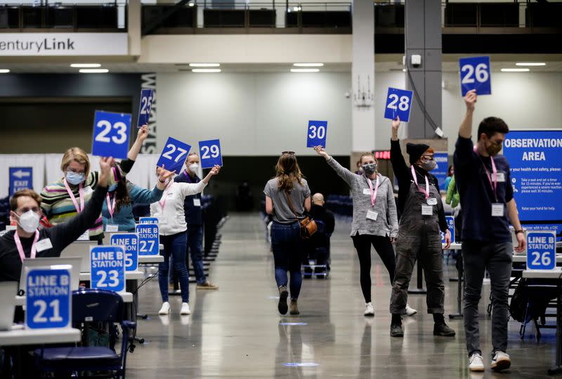 Workers hold up their station signs to signal they are ready for a patient as people attend a coronavirus disease (COVID-19) vaccination site at Lumen Field Event Center in Seattle