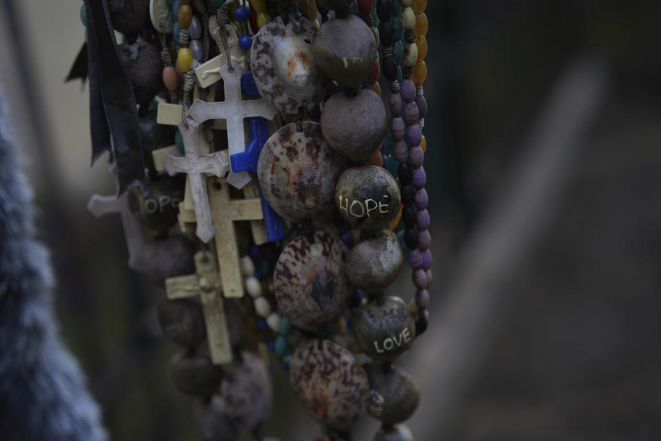 Necklaces, shells and crosses hang from the grave of Father Damien outside of St. Philomena Church on Kalaupapa, Hawaii, on Tuesday, July 18, 2023. Damien was canonized a Catholic saint in 2009 for his work taking care of the physical and spiritual needs of leprosy patients in the 1800s. His body was moved to his home country of Belgium in 1936. Only the priest's hand remains, which was reburied at the site in 1995. (AP Photo/Jessie Wardarski)