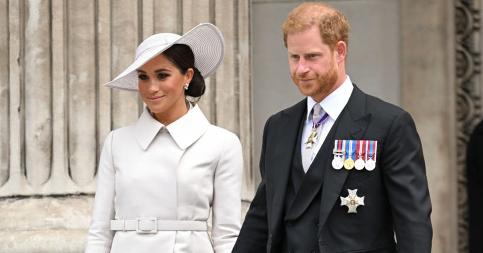 Meghan in a large white hat and white jacket, Harry in a black suit jacket with royal medals on the lapel