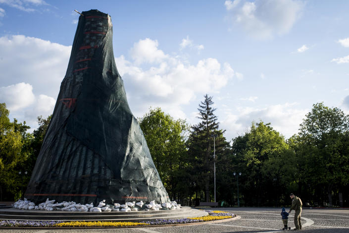 A child and a man in a military uniform pass a monument to Ukrainian Poet Taras Shevchenko that has been surrounded by protective sandbags on May 18, 2022, in Kharkiv. (Pete Kiehart for NBC News)