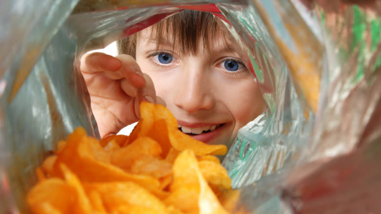 Child peering into a bag of potato chips