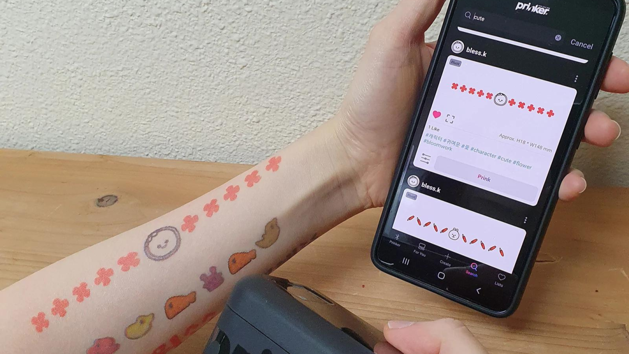 arm covered in temporary tattoos holding phone with Prinker app