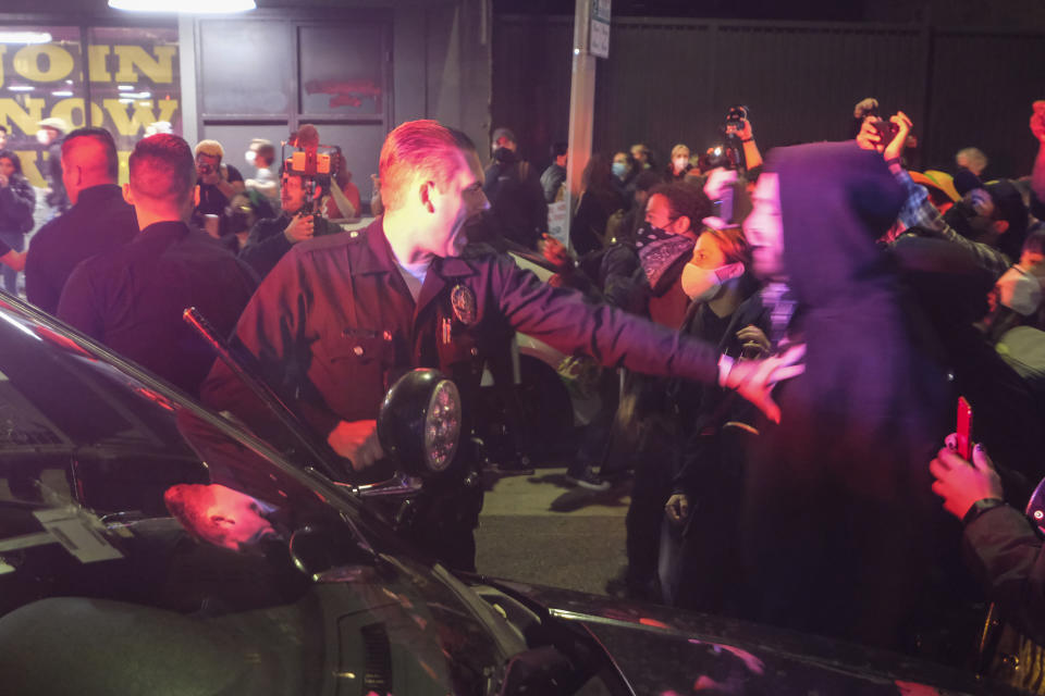 A police officer angrily stretches out his arm to push back a protester in a hoodie, with other demonstrators in the background.