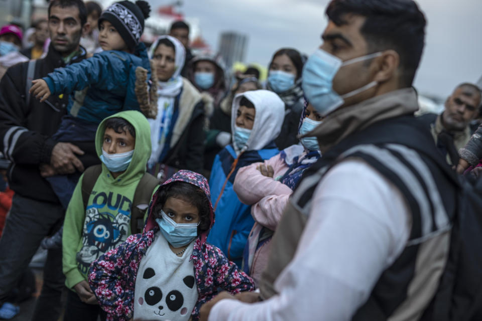 Refugees and migrants wearing masks to prevent the spread off the coronavirus, wait to get on a bus after their arrival at the port of Piraeus , near Athens, on Monday, May 4, 2020. Greek authorities are moving 400 migrants, mostly families, to the mainland to help ease overcrowded conditions at the camp Moria in Lesbos island. (AP Photo/Petros Giannakouris)