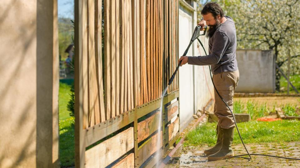 Man cleaning a wooden gate with a power washer. 