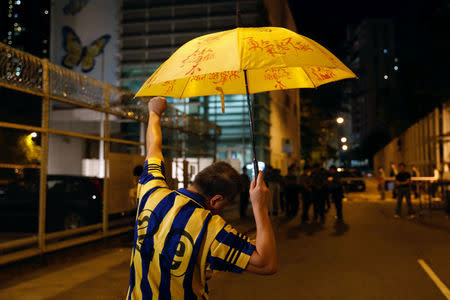 A protester holds a yellow umbrella, the symbol of the Occupy Central movement, in support of jailed Hong Kong student leaders Joshua Wong, Nathan Law and Alex Chow, while officers from the Correctional Services Department stand guard outside a prison in Hong Kong, China August 18, 2017. REUTERS/Tyrone Siu