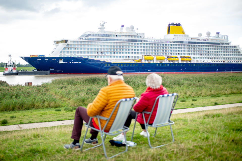 30 August 2020, Lower Saxony, Westoverledingen: A couple sits on two chairs on the dike near the village of Dorenburg and looks at the new cruise liner "Spirit of Adventure", which has left the Meyer shipyard and is sailing on the Ems. The ship built for the British shipping company Saga Cruises is to be transferred to the North Sea via the Ems. Photo: Hauke-Christian Dittrich/dpa (Photo by Hauke-Christian Dittrich/picture alliance via Getty Images)