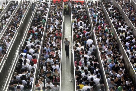 A security officer stands guard as passengers line up and wait for a security check during morning rush hour at Tiantongyuan North Station in Beijing