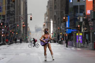 Street performer Robert John Burck, known as The Naked Cowboy, poses for photos in New York's Times Square, Thursday, April 9, 2020, during the coronavirus epidemic. He is wearing a mask and his guitar is adorned with stickers that read, "Trump Keep America Great." The New York City immortalized in song and scene has been swapped out for the last few months with the virus version. In all the unknowing of what the future holds, there's faith in that other quintessential facet of New York City: that the city will adapt. (AP Photo/Mark Lennihan)