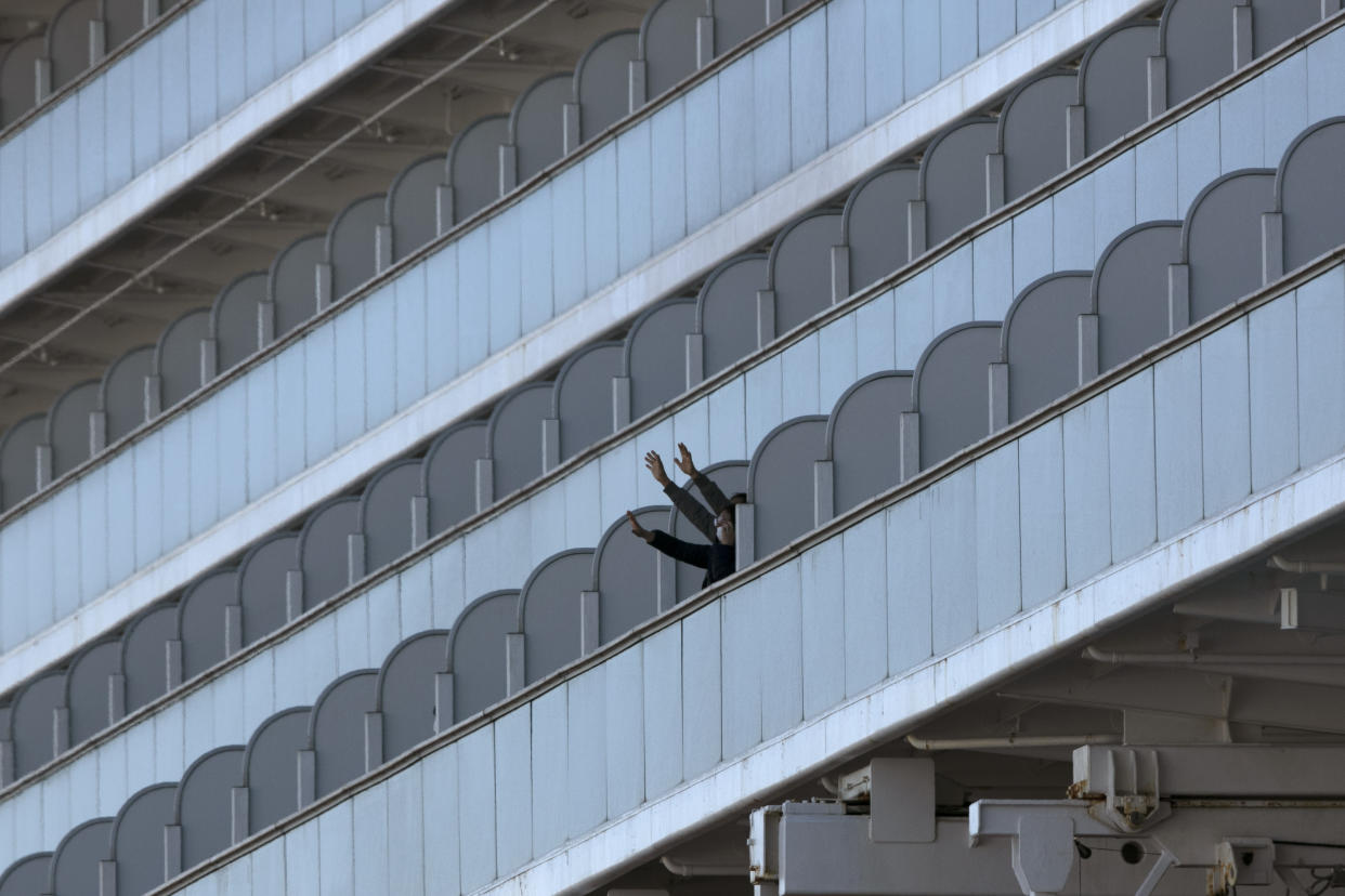 Two people wave from the quarantined Diamond Princess cruise ship in Yokohama, near Tokyo, Tuesday, Feb. 11, 2020. Japan's Health Minister Katsunobu Kato said the government was considering testing everyone remaining on board and crew on the Diamond Princess, which would require them to remain aboard until results were available. (AP Photo/Jae C. Hong)