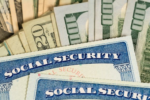 Two Social Security cards lying atop fanned stacks of cash bills.