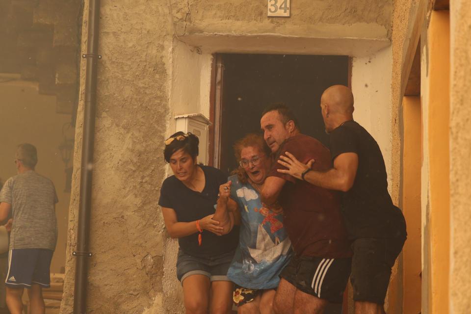 A woman is helped out of a house by neighbours in Anon de Moncayo, Spain on Saturday Aug. 13, 2022. A large wildfire in northeast Spain grew rapidly overnight and was burning out of control. It has already forced the evacuation of eight villages and 1,500 people in Zaragoza province. A local government official said Sunday that the situation was critical in the town of Añon de Moncayo and the priority for the 300 firefighters fighting the blaze was to protect human lives and villages. (Fabian Simon/Europa Press via AP)