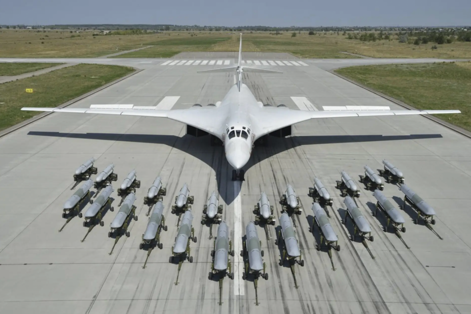 A row of 12 Kh-101/102-series air-launched cruise missiles, in front, and another dozen of the earlier Kh-55-series missiles behind them, on display with a Tu-160 Blackjack bomber in the background. <em>Russian Ministry of Defense</em>